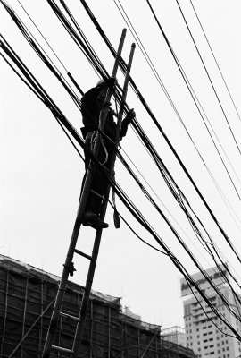 Repairs to the electrical wiring are often made with rather little precautions. A wooden ladder leaning against the wires, a hemp rope and the work can begin. 
Far from being a rare sight, this is how things are done in Shanghai. Similar methods are used for cleaning the facades of skyscrapers and more.