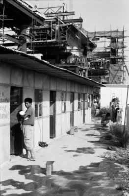 A migrant worker holds his infant during a break. This house holds maybe twenty workers, their families, and belongings. Looming in the back is a bridge over a local road. The families cook here, wash their veggies out back and move as the construction moves along the track.