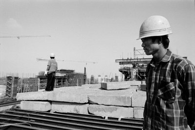 Two workers stand atop a concrete pillar of the maglev they are building. Each of these pillars supports a giant concrete and steel piece that two tracks are laying on. The workers live on site, in a makeshift shack just down the ramp with their wifes and small children.