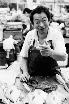 The wet market is full of fish in basins, or already gutted and ready to take home. This man was happily bantering with me, although his hand never left his knife on the table. In front, pomfret are lined up on the wooden counter and his arms and clothes are full of scales.