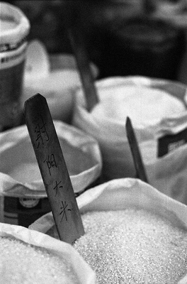Rice bags with neat labels made from thin slices of wood, denoting the type and origin form a simple composition of circles and diagonals. 

This stall was by far the cleanest and best arranged in the entire market and its Japanese proprietor proud, but also camera shy. 