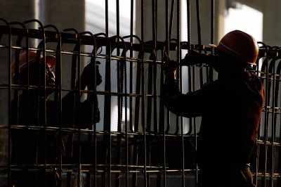 Two workers are busy with some more steel, this time shot in back light, against the pillars of concrete already done. 

I like the eyes and the expression of the man on the left. He is focused on his work, which seems and endless daunting task of tying steel and then doing it all over again tomorrow.