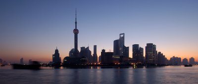 The sun rises behind the skyline of Pudong in Shanghai. The river is already busy with traffic and the lights from the office buildings blend with the sunrise. 
