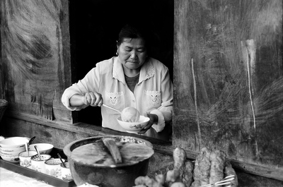 Pouring a bowl of congee, the owner of this well assorted breakfast place by the market in Heshun, looks out on the center of the market every day. 

Serving congee, you tiao, and spicy noodles, the place is a favorite with the locals.
