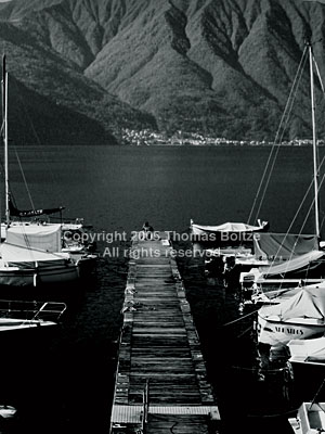 The old wood on the boat landing on the Lago di Como shines in the sunshine, while the lake lies black, awaiting a summer.